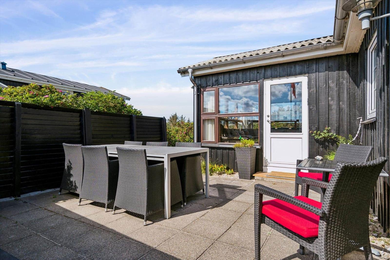 Terrasse mit Tisch und Stühlen vor einem Haus mit weißer Tür.