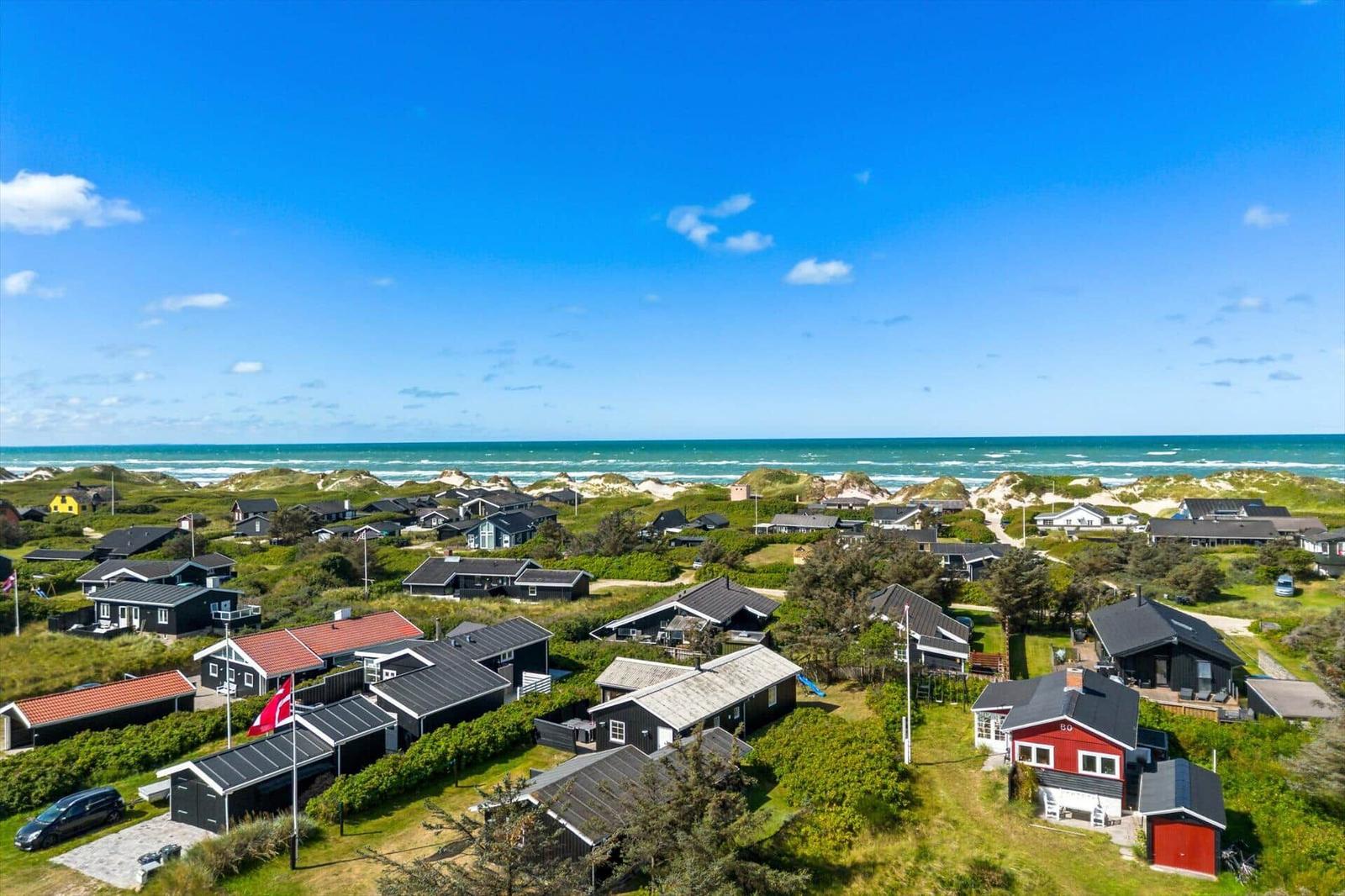 Meerblick auf Strandhäuser mit Dünen und blauem Himmel.