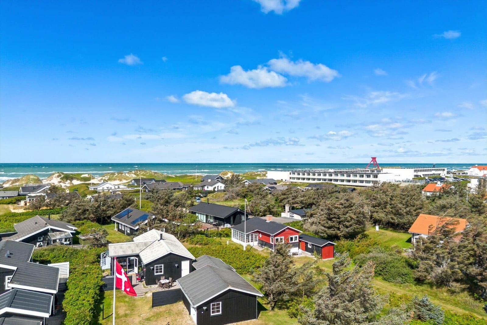 Meerblick mit Strand, Dünen und Häusern unter blauem Himmel mit weißen Wolken.