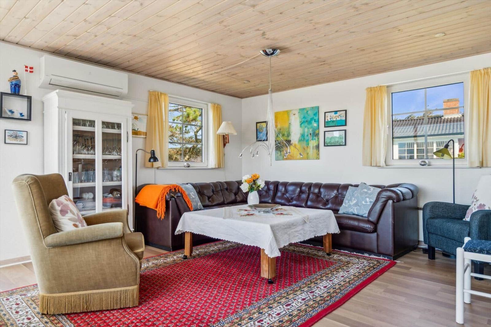 Wohnzimmer mit braunem Ledersofa, rotem Teppich und Holzboden. Fenster mit gelben Vorhängen.