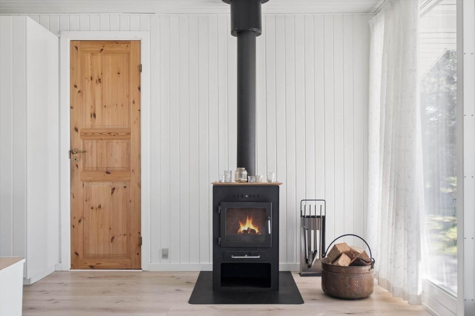 Wood stove with firewood, wooden door, and window with curtain.