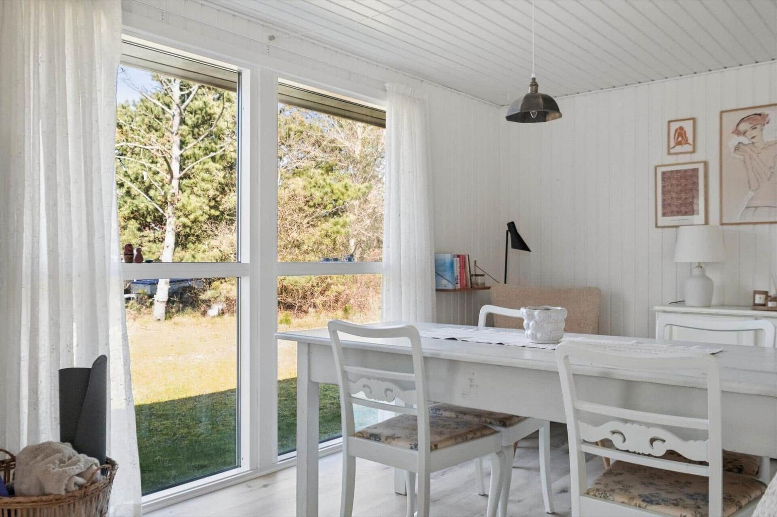 Dining room with white table and chairs. Large windows show a garden.