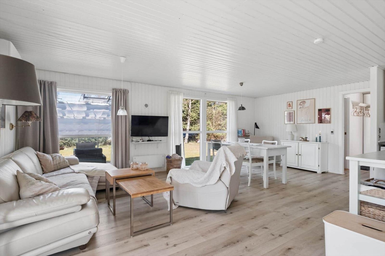 Living and dining area with sofa, dining table, and windows. Wooden floor and white walls.