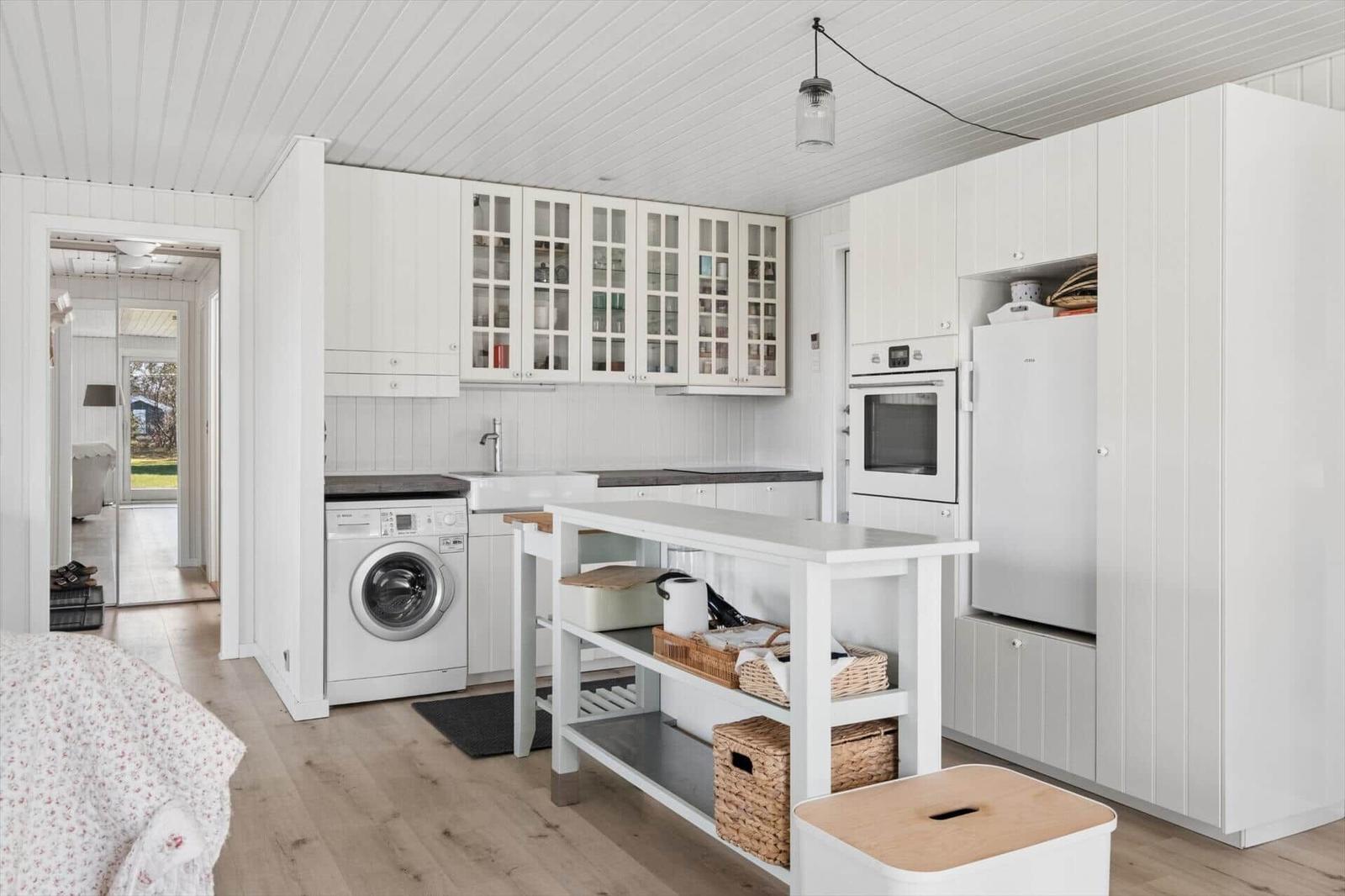 Kitchen with white cabinets, washing machine, refrigerator, and island with baskets.