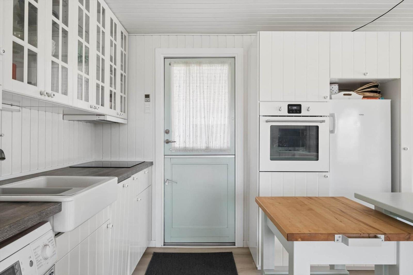 Kitchen with white cabinets, wooden table, and door with grid window.
