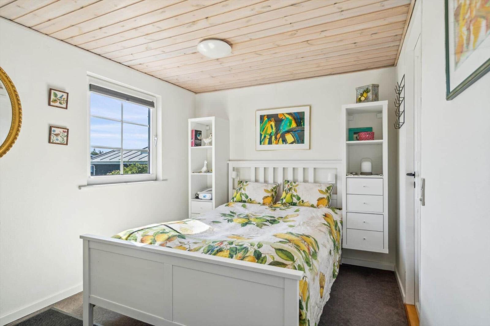 Schlafzimmer mit Bett, Fenster und weißen Schränken.