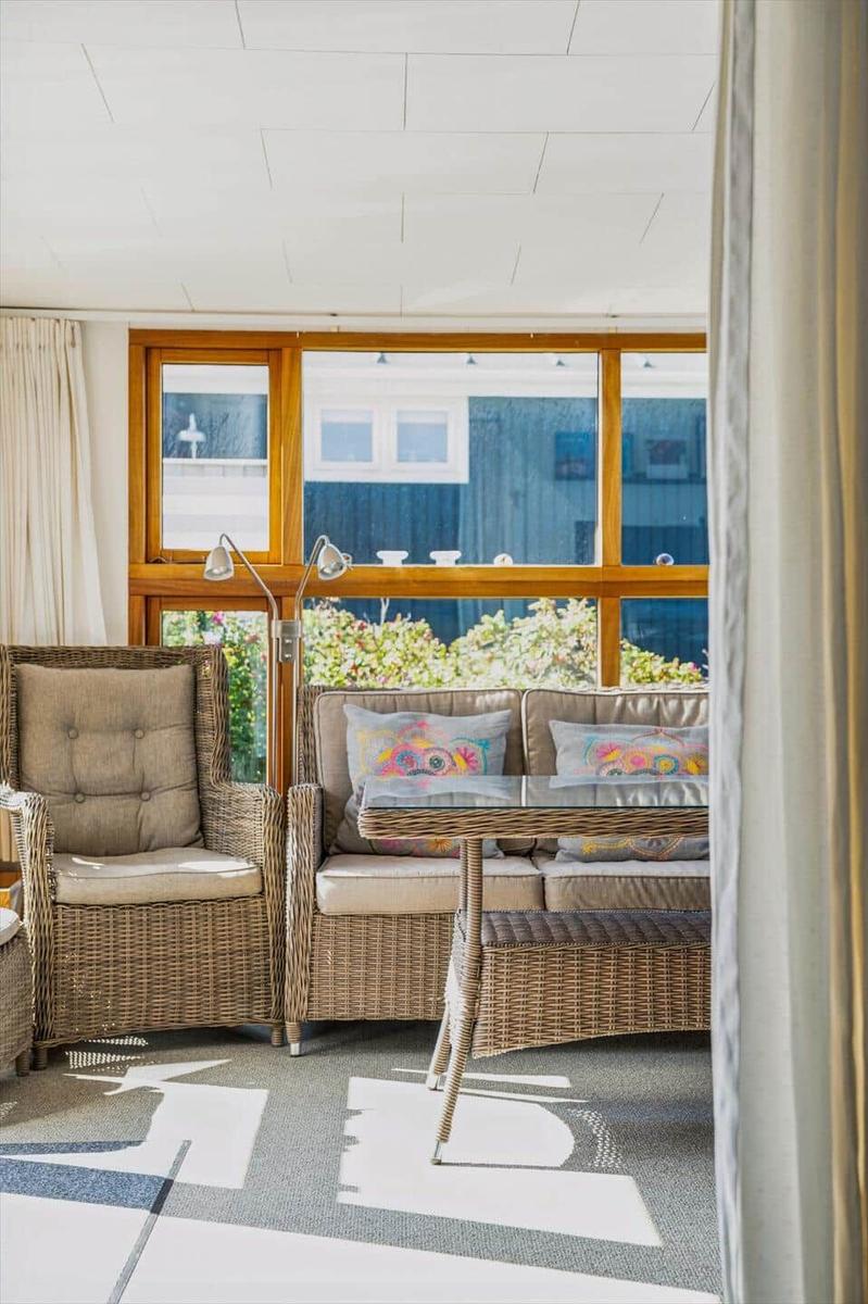 Wohnbereich mit Rattanmöbeln, Glas-Tisch und großem Fenster mit Blick auf Garten.
