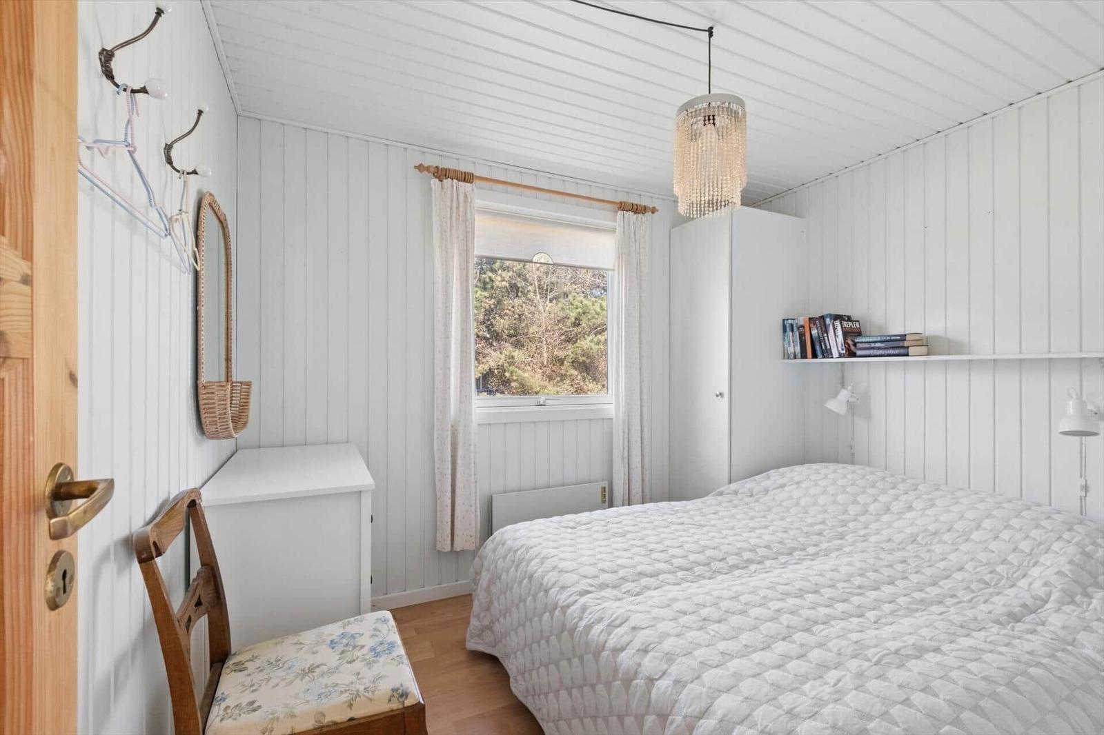 Bedroom with bed, window, closet, and chair. Ceiling and walls are white paneled.