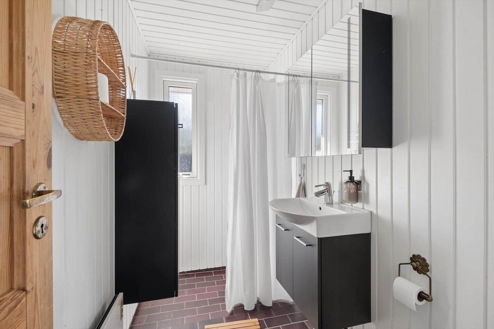 Bathroom with sink, shower curtain, and wall mirror. Wood and basket decor.