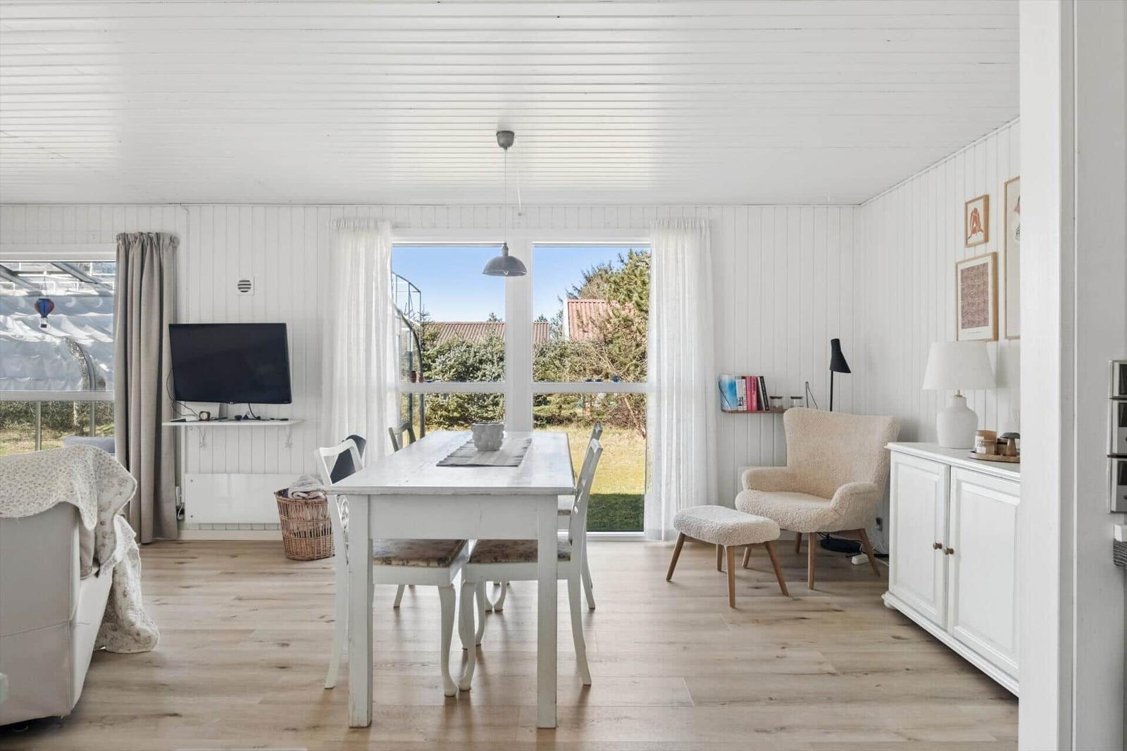 Living and dining area with white table, chairs, and windows to the garden.