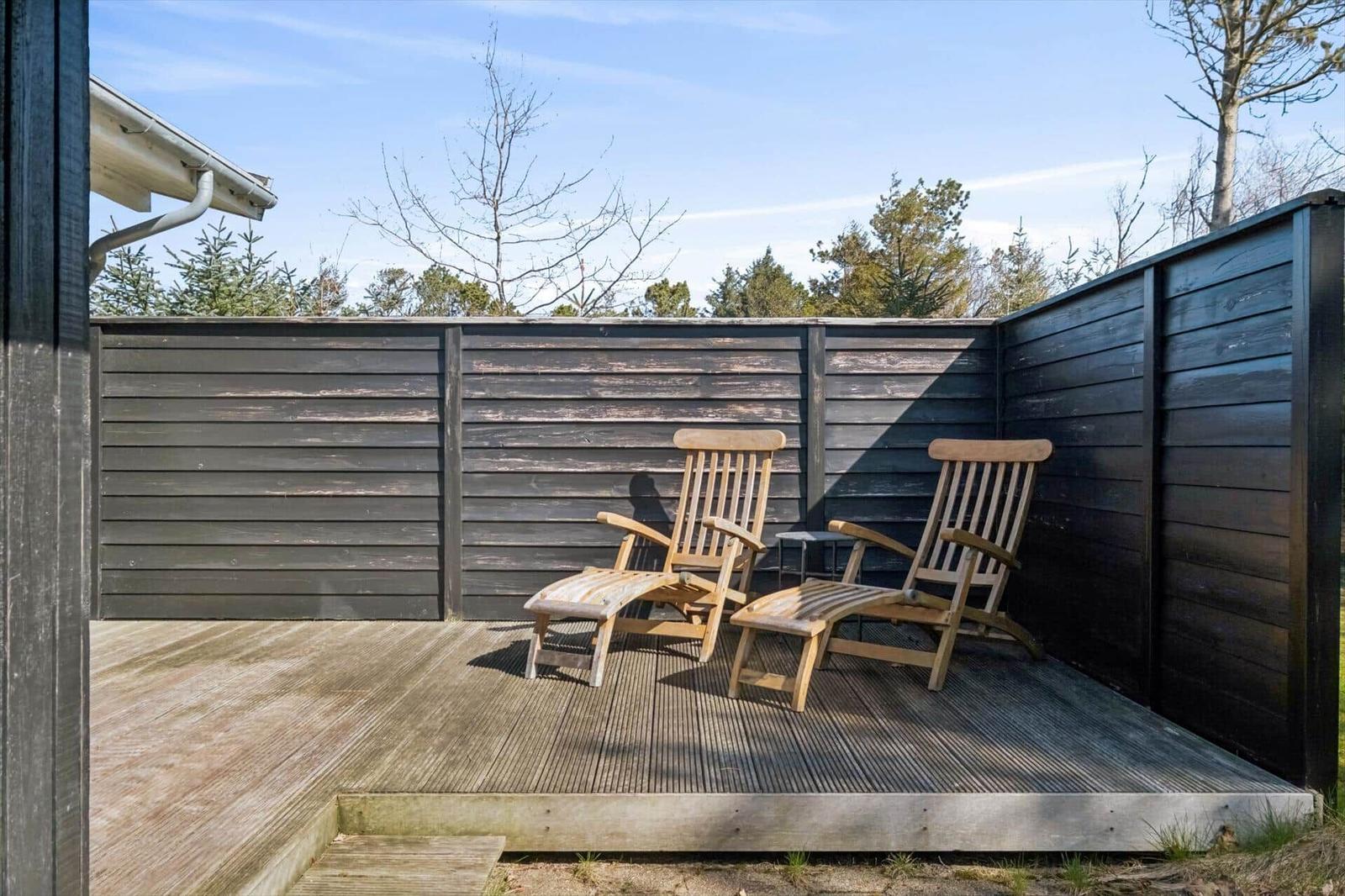 Terrace with two wooden loungers and dark wood railing. Background: trees and clear sky.