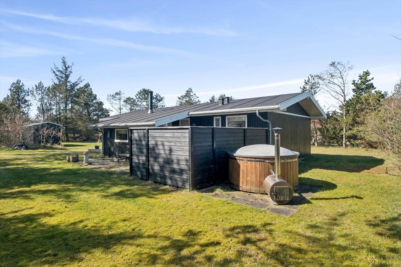 A house with wooden cladding and an outdoor tub. Surrounded by grass and trees.