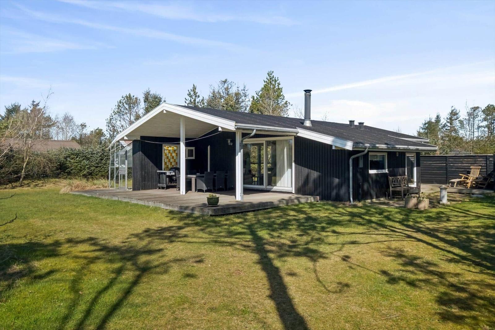Modern wooden cabin with terrace, grill, and garden. Surrounded by trees and grass.