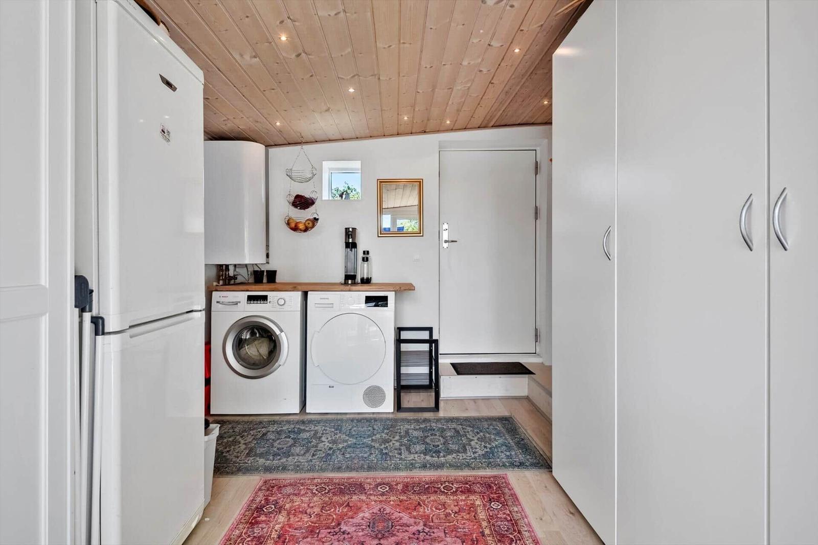 Kitchen with fridge, washing machine, and dryer. Wooden ceiling and rugs.