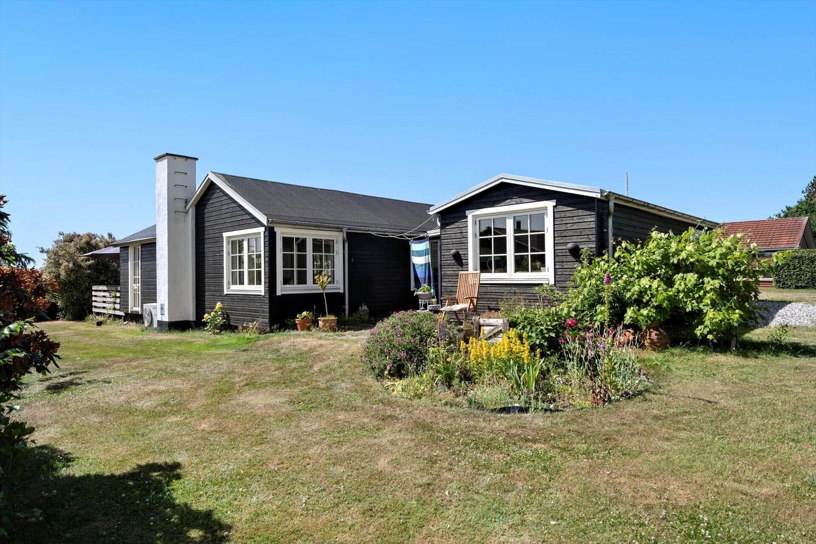 Black wooden house with white windows and garden with flowers.
