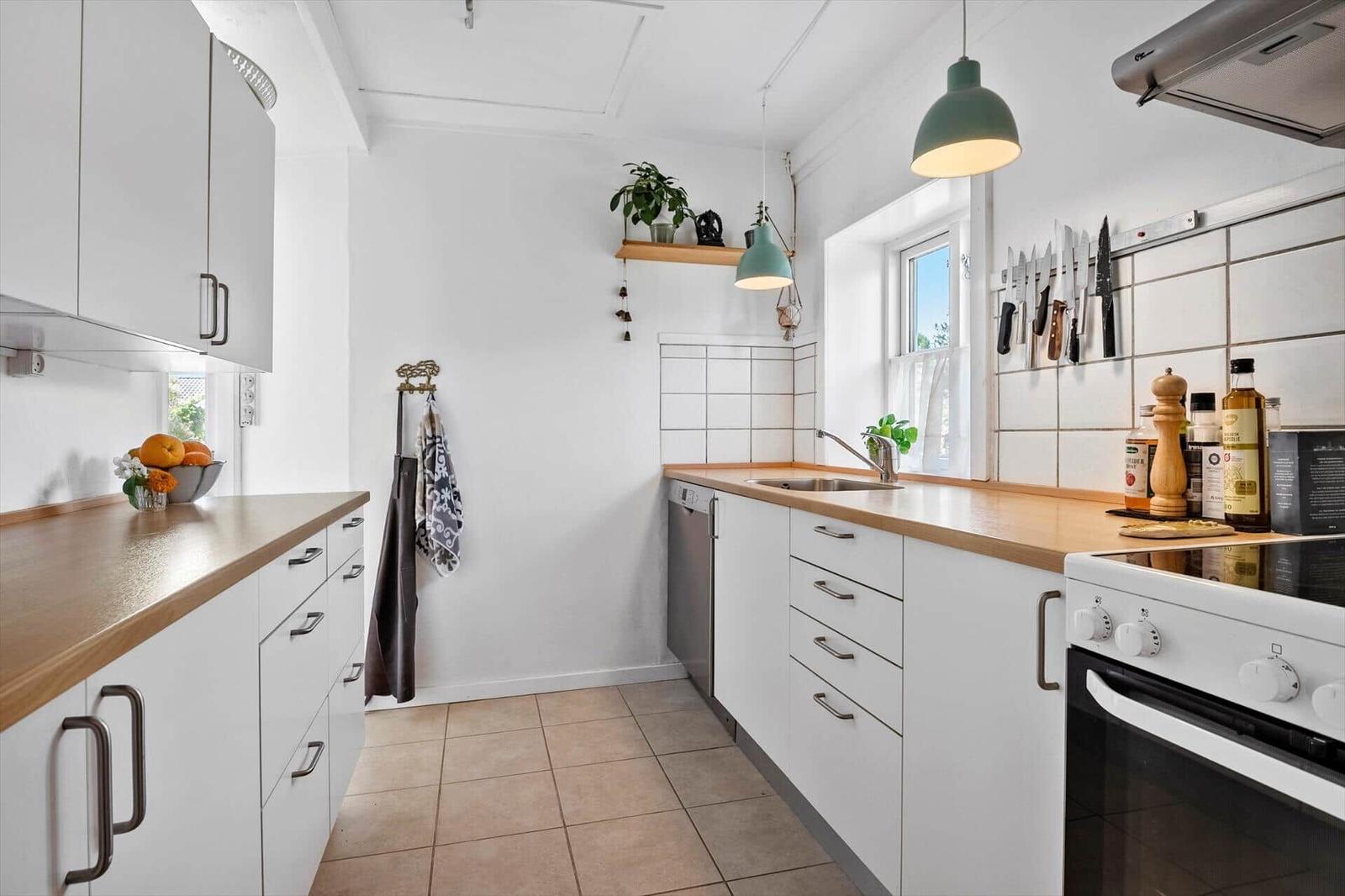 Kitchen with white cabinets, wooden countertops, and a window. Kitchen utensils hang on the wall.