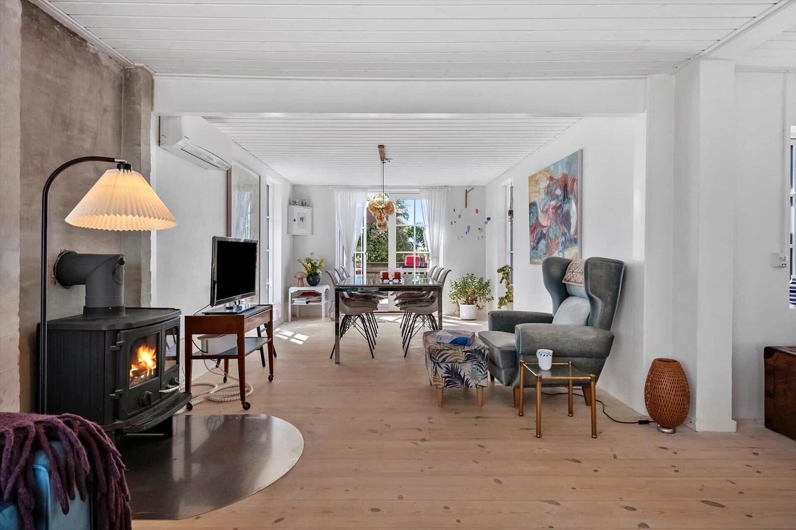 Living and dining area with fireplace, armchair, and table. Wooden floor and light walls.