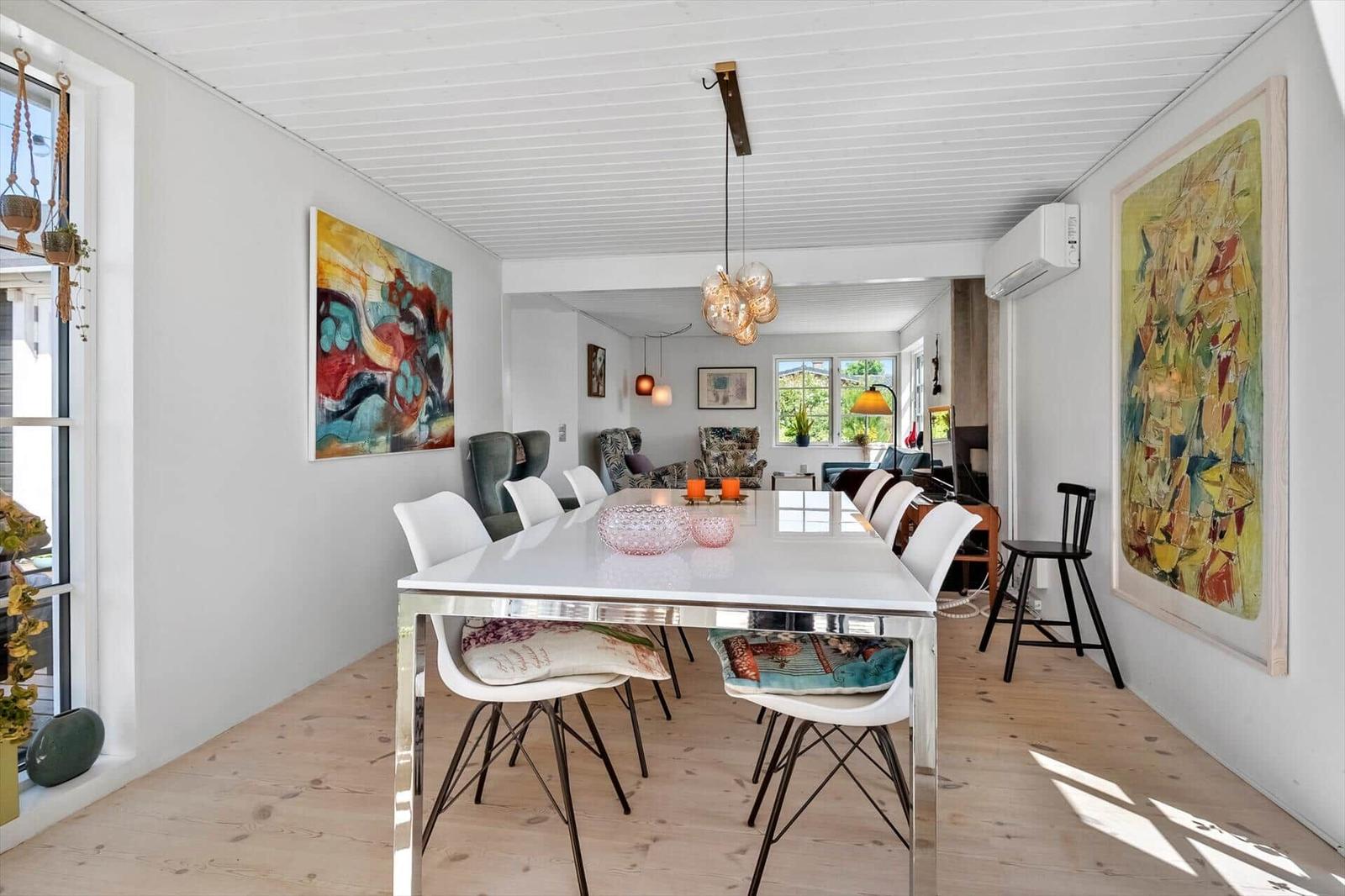 Dining room with white table, white chairs, and large wall artworks. Wooden floor and light-colored walls.