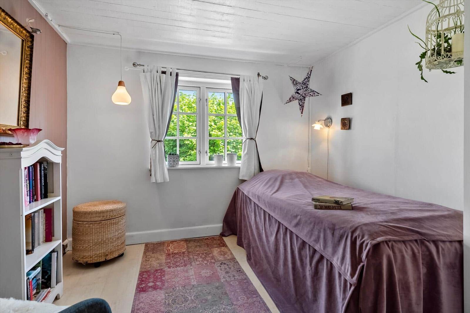 A bedroom with bed, window, bookcase, and ceiling fan.