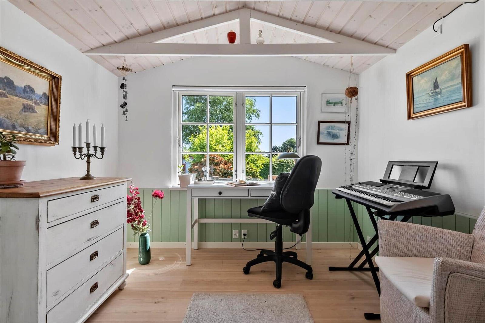 A workspace with desk, chair, and keyboard. Window with view of greenery. Wooden floor and wainscoting.