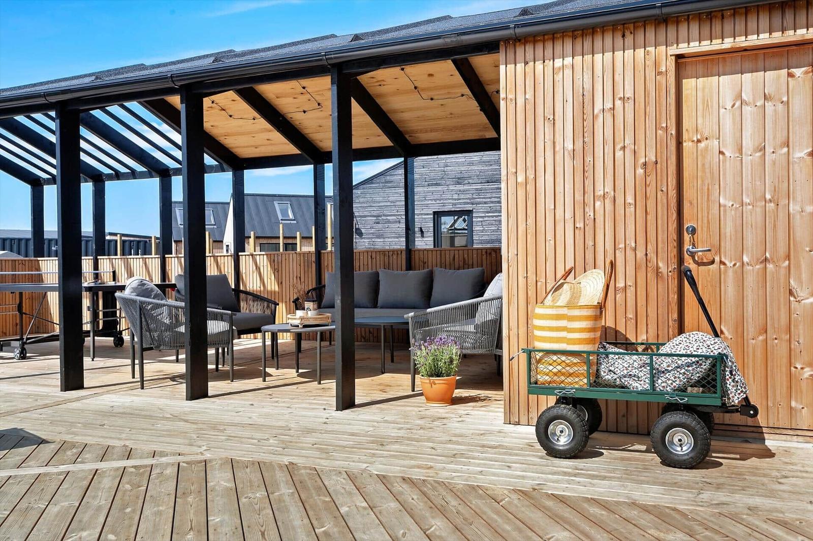 Terrasse mit Sitzgruppe, Holzdecke und Gartenwagen vor Holzhütte.