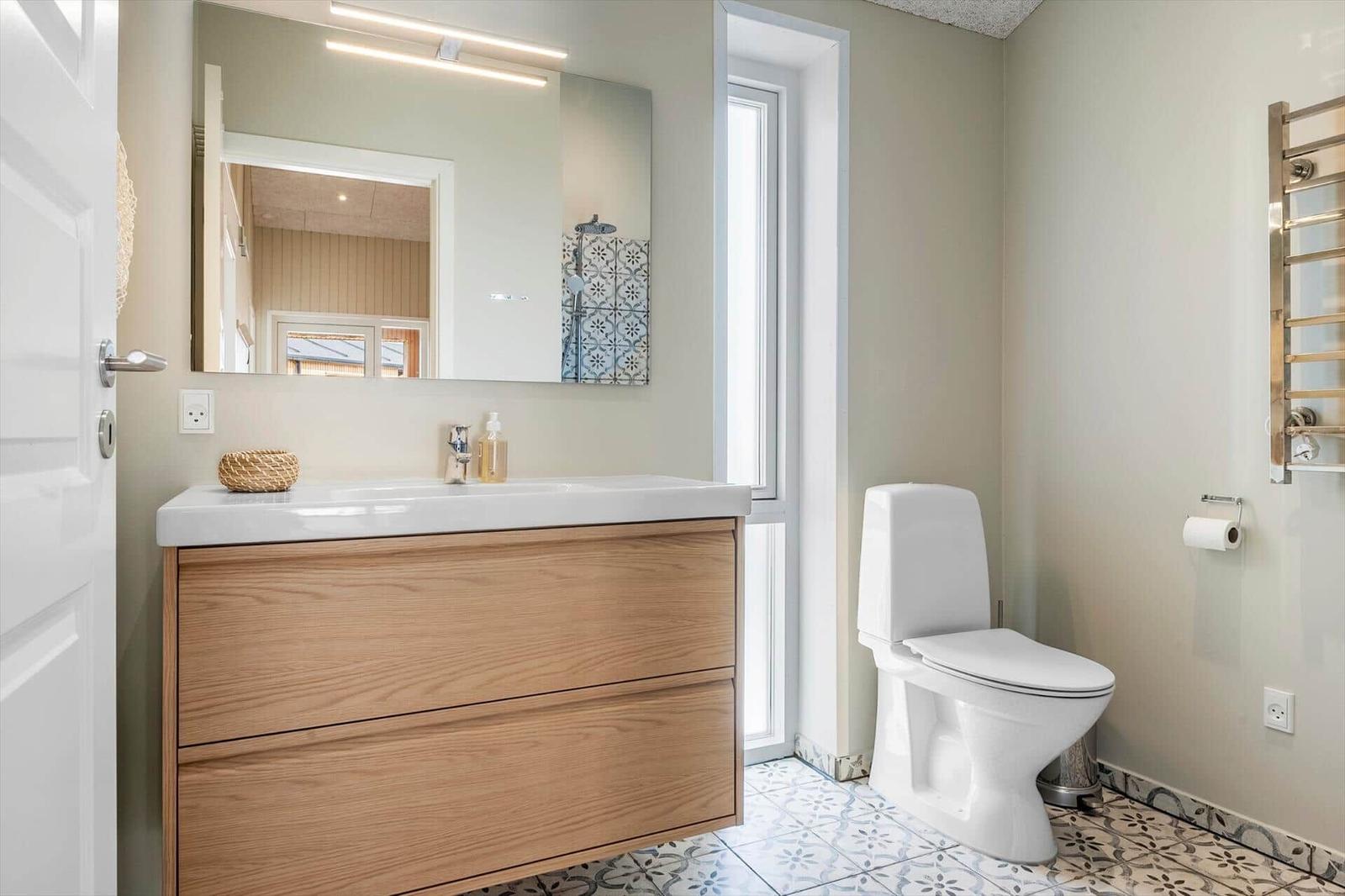 Badezimmer mit Waschbecken, Spiegel und Toilette. Fliesenboden und Holzschrank.