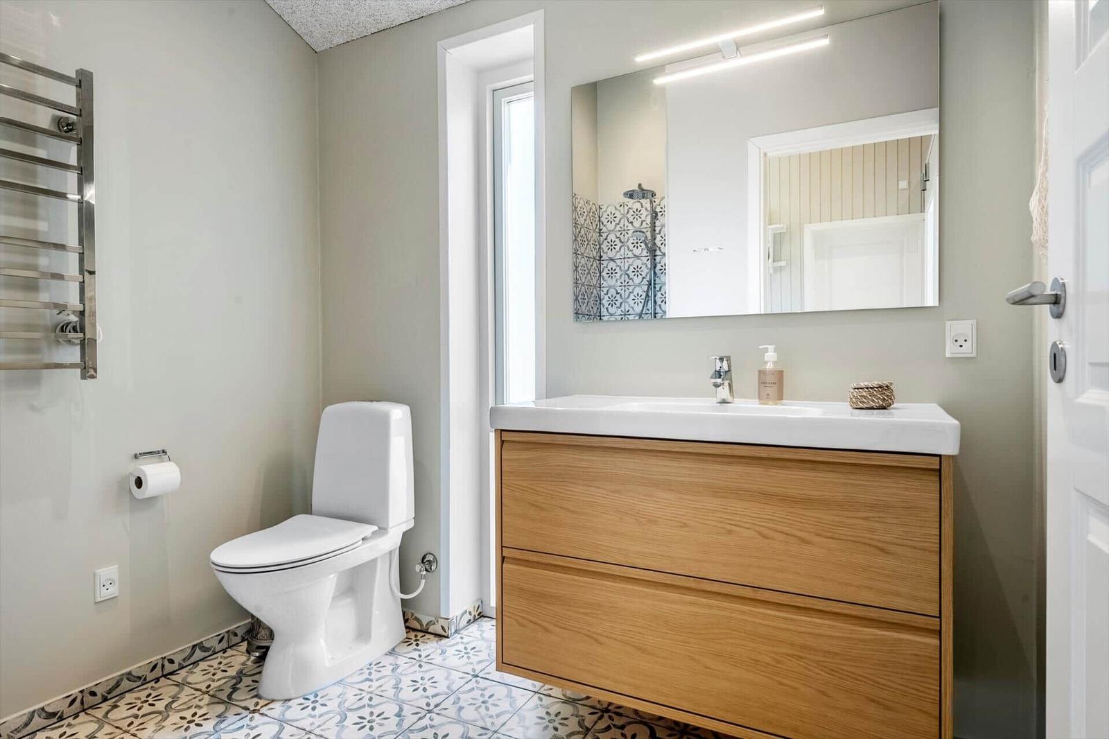 Badezimmer mit Toilette, Waschbecken und Spiegel. Fliesenboden und Holzschrank.
