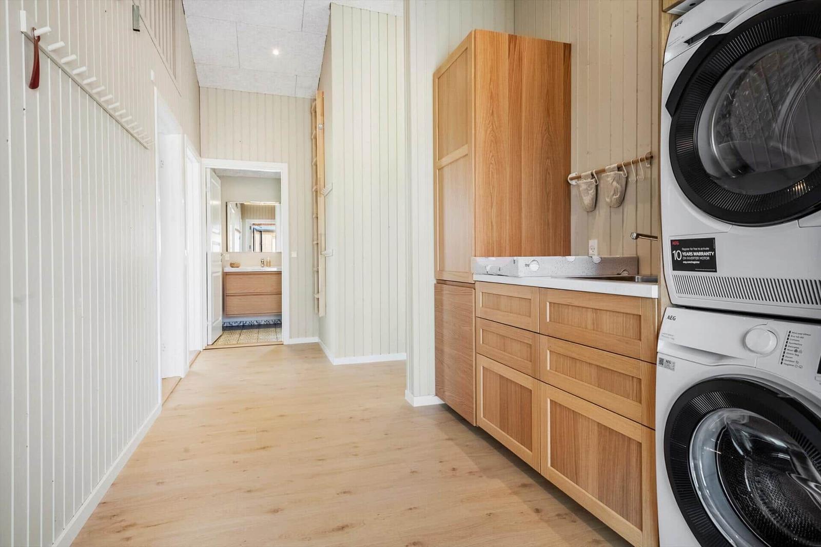 Wohnung mit Waschmaschine, Trockner und Holzmöbeln. Flur führt in das Badezimmer.