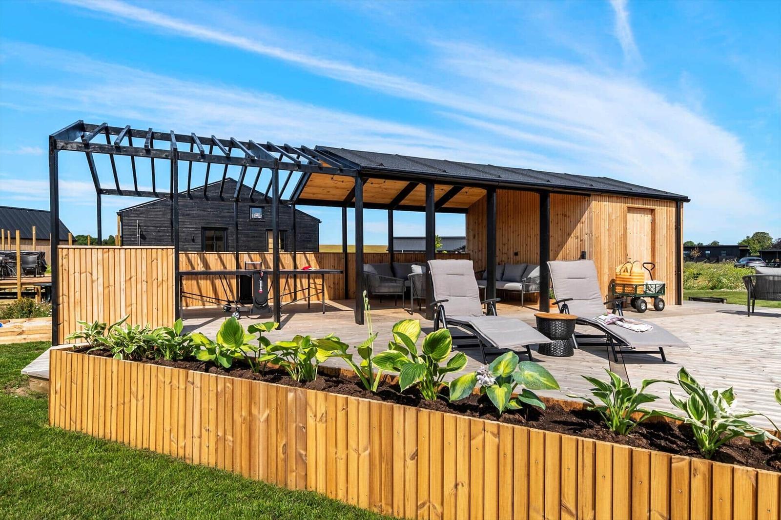 Terrasse mit Liegen, Sitzgelegenheiten und Pergola unter blauem Himmel.