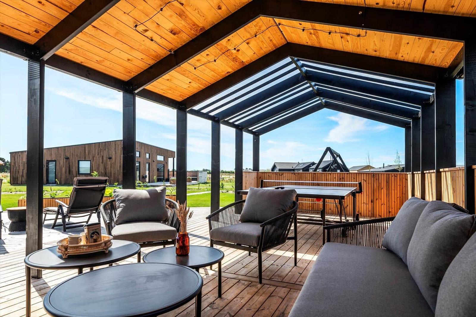 Terrasse mit Sitzgruppe, Tischen und Holzdecke unter freiem Himmel.