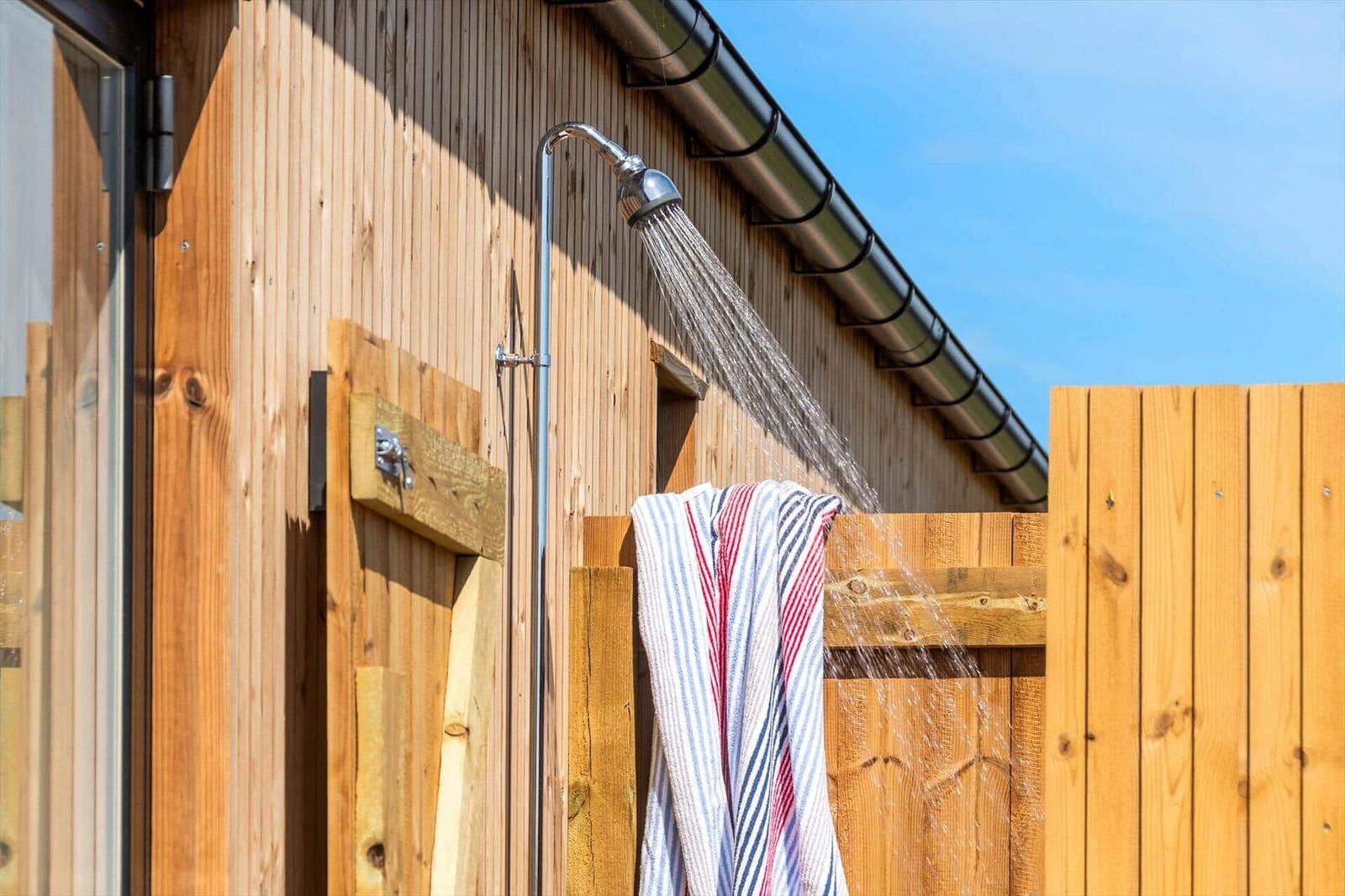 Außen-Dusche mit Wasserstrahl, Handtuch hängt an Holzgeländer.
