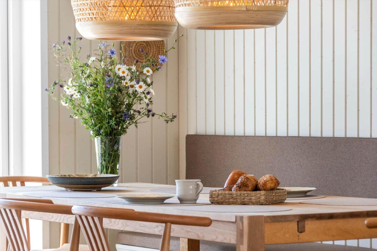 Esstisch mit Stühlen, Blumenstrauß und Brot im Hintergrund.