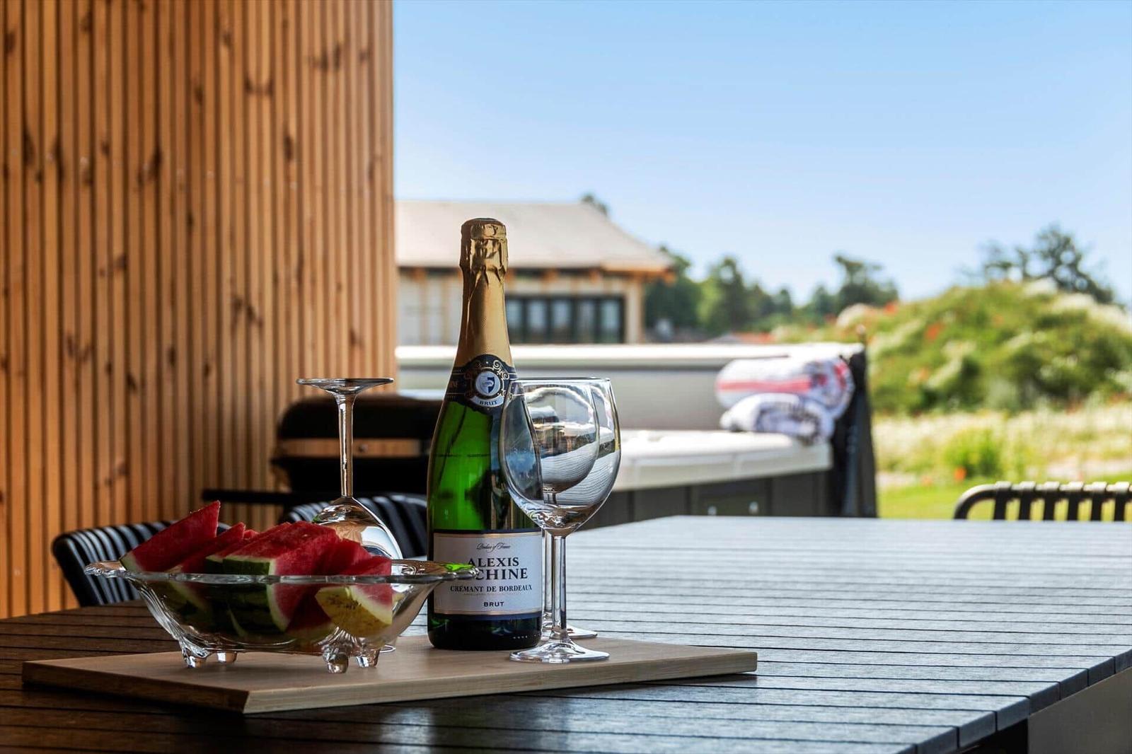 Auf der Terrasse steht ein Tisch mit einer Flasche Champagner, zwei Gläsern und einer Schale Wassermelone.