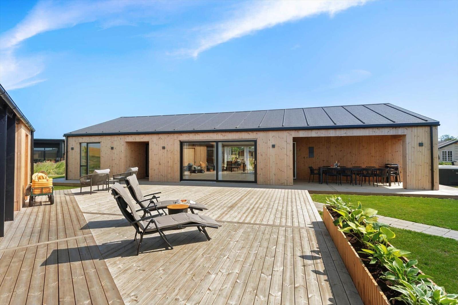 Moderne Holzhütte mit großem Balkon, Liegestühlen und Essbereich im Freien.