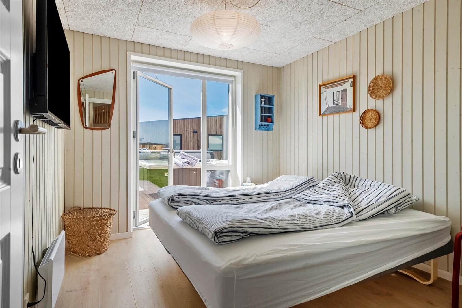 Schlafzimmer mit Bett, TV und Balkontür. Wände mit vertikalen Paneelen.