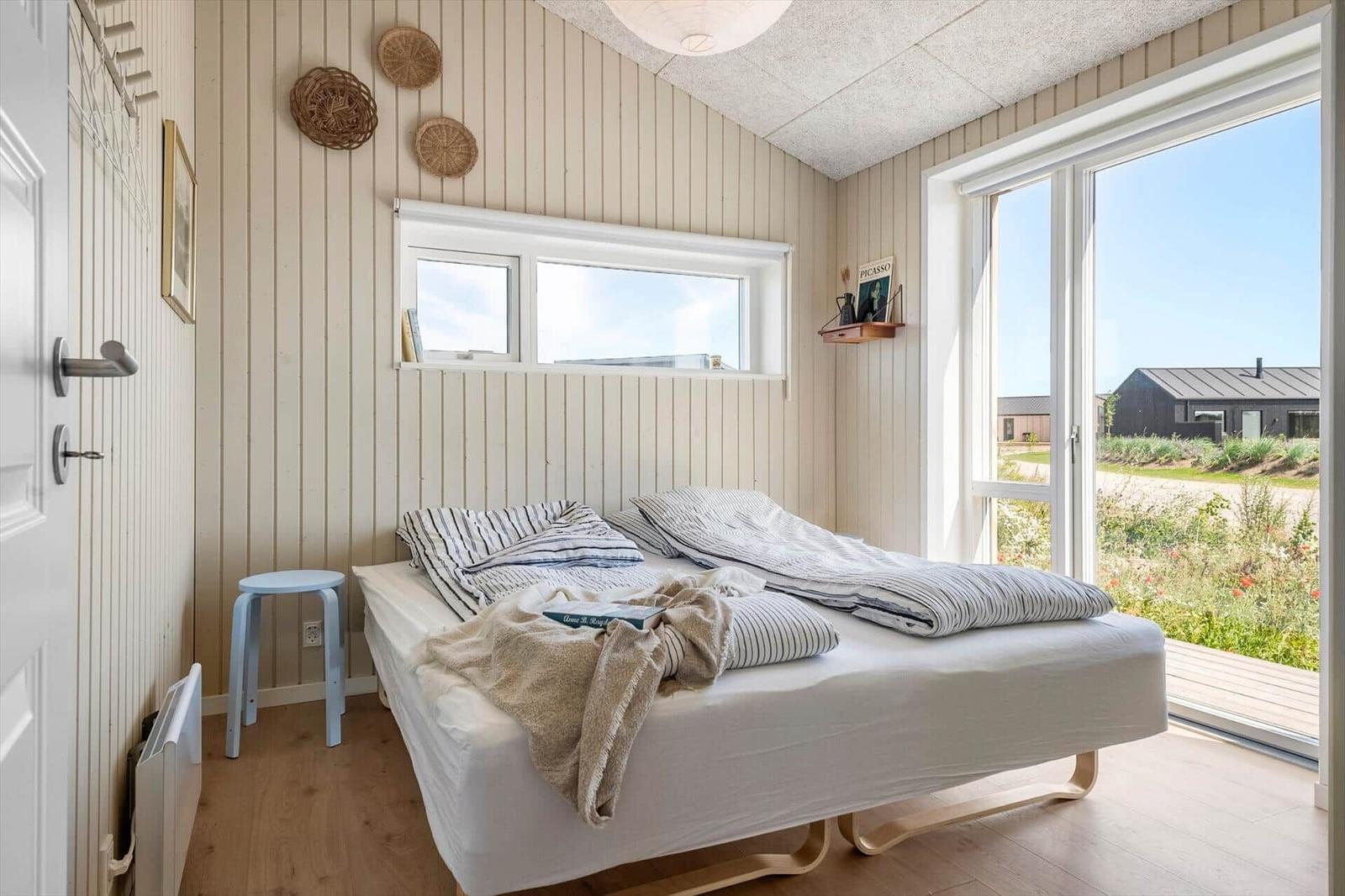 Schlafzimmer mit Bett, Fenster und Tür zum Balkon. Holzwände und helles Ambiente.