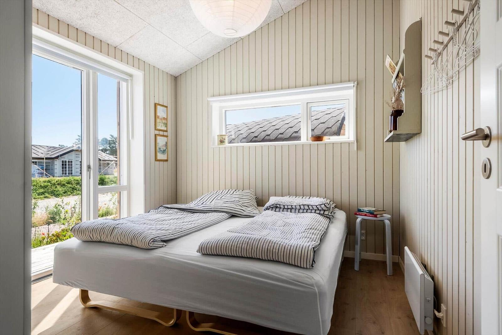 Schlafzimmer mit Bett, Fenstern und Holzboden. Anblick auf Dach und Garten.