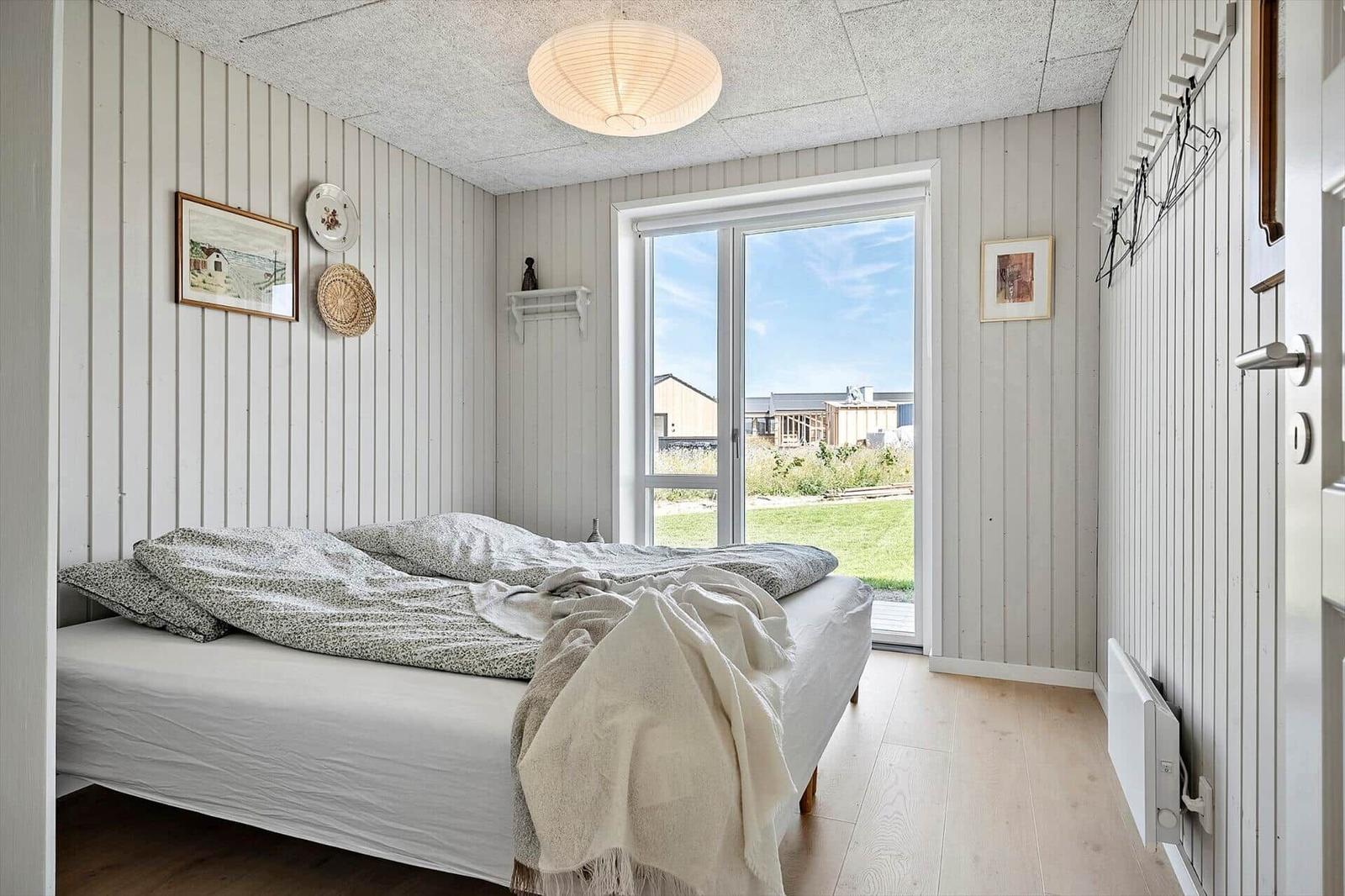 Bedroom with bed, window, and wooden floor. Walls with vertical panels.