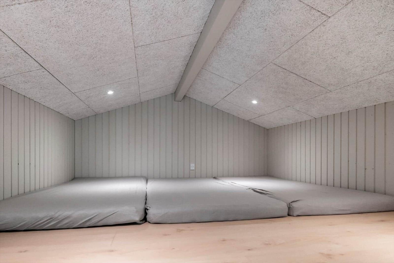 Room with two mattresses on wooden floor and vertically paneled walls.