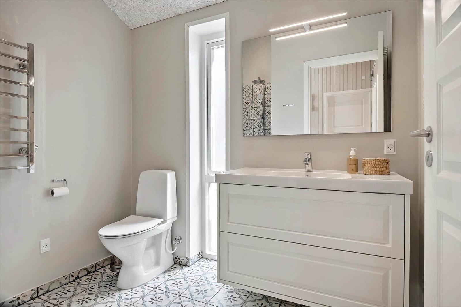 Bathroom with toilet, sink and mirror. Tile floor and heater on the wall.