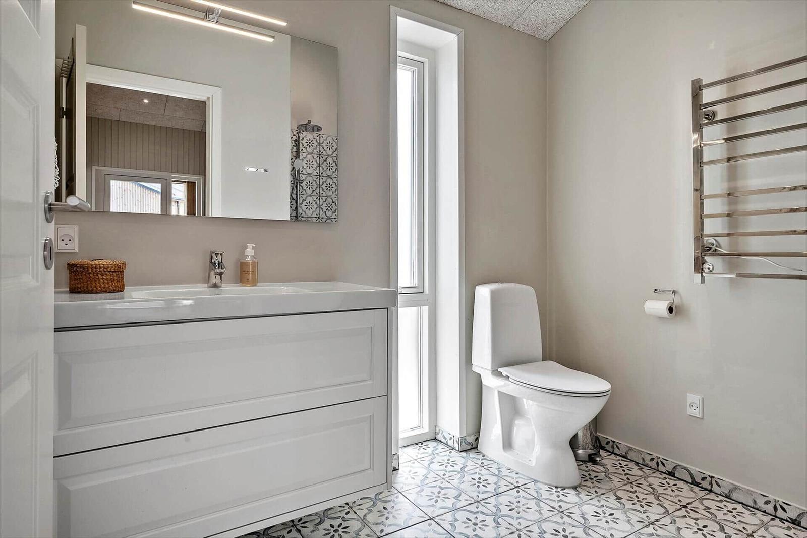 Bathroom with sink, toilet, and heater. Tile floor and mirror with light.