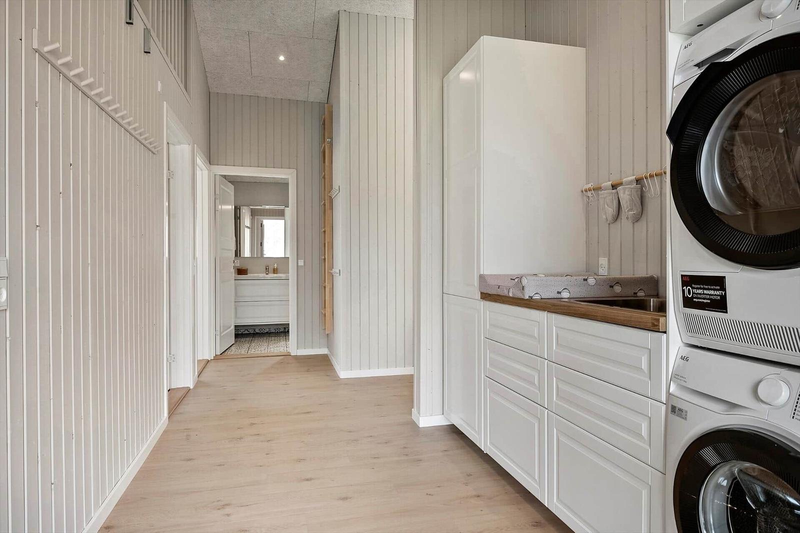 Laundry room with washer and dryer, white cabinets, and wooden floor. Hallway leads to the bathroom.