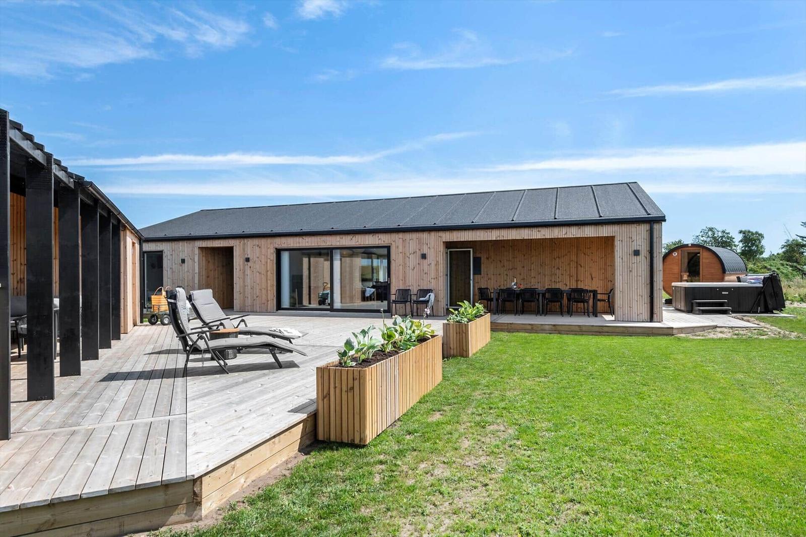 Modern wooden house with terrace, loungers, and garden. Adjacent building with hot tub.