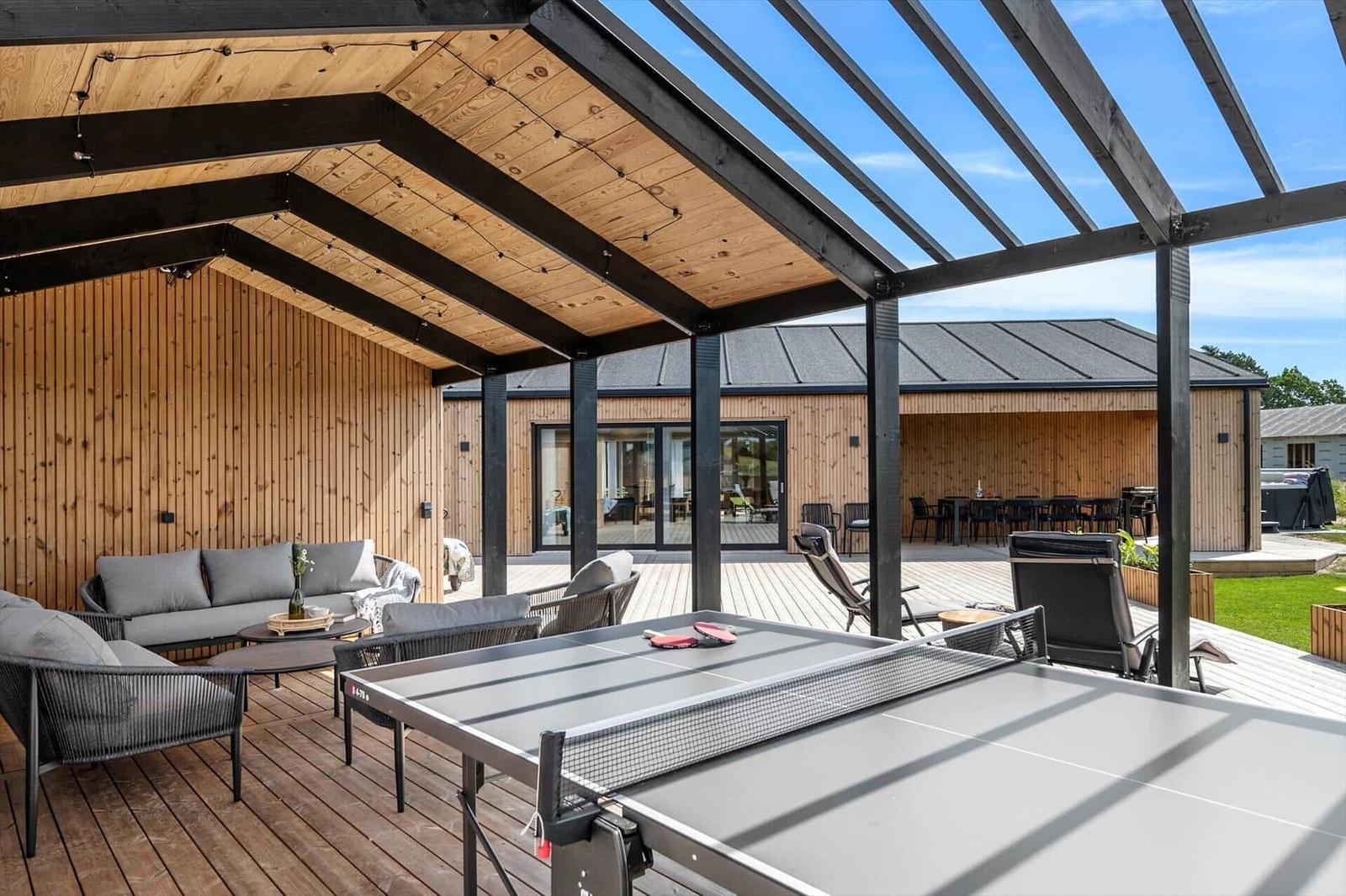 Outdoor area with ping pong table, seating, and wooden veranda under roof.