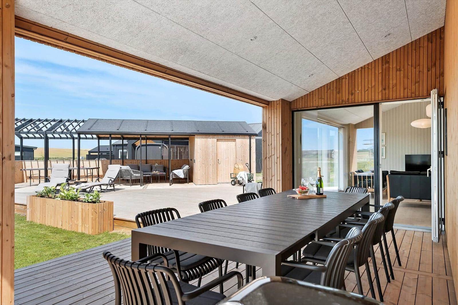 Large covered terrace with table and chairs. View of patio and garden.