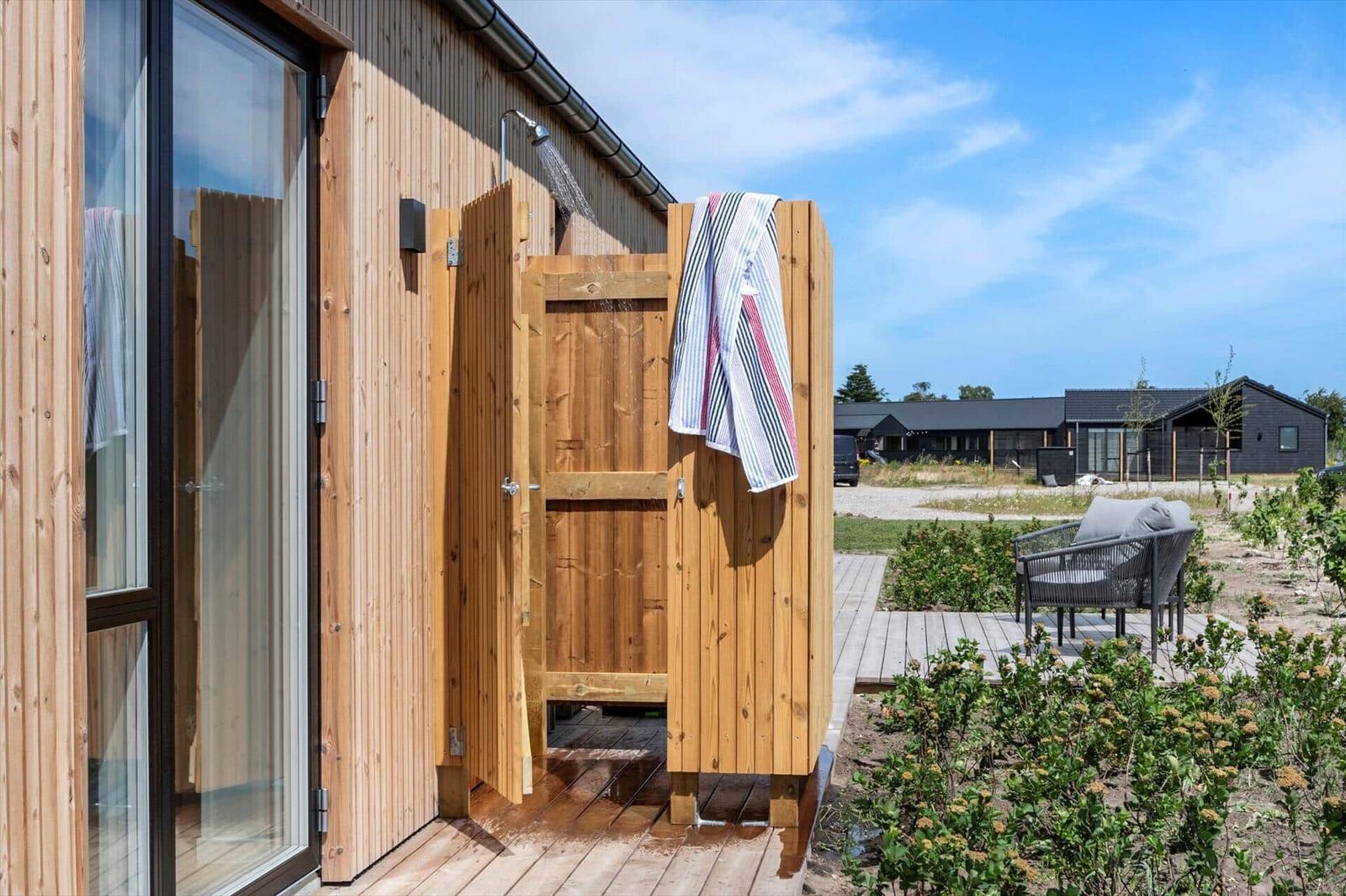 Outdoor wooden shower with towel, next to terrace and garden
