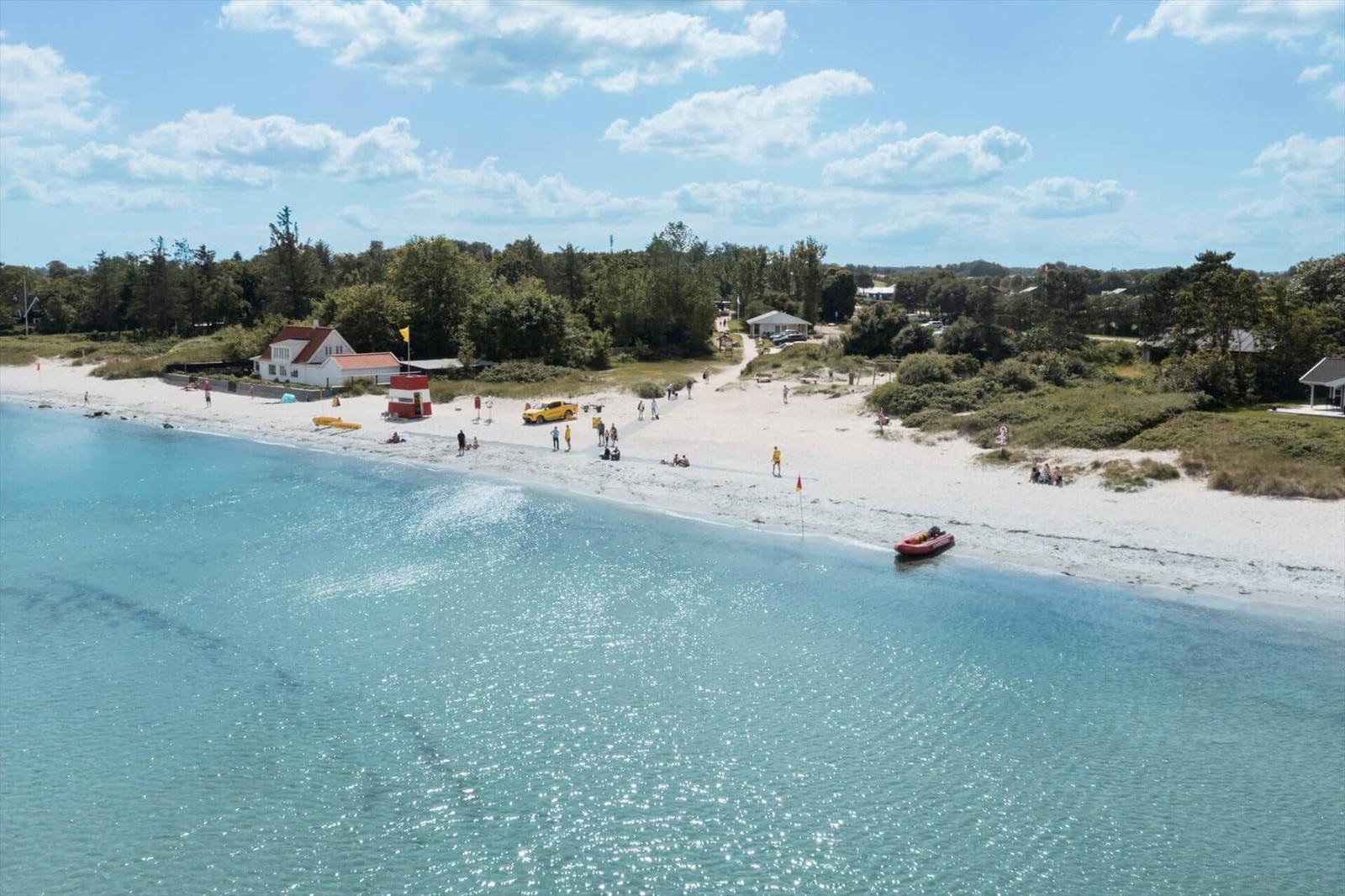 Beach with white sand, turquoise water, and some people. A red rescue boat is on the shore.
