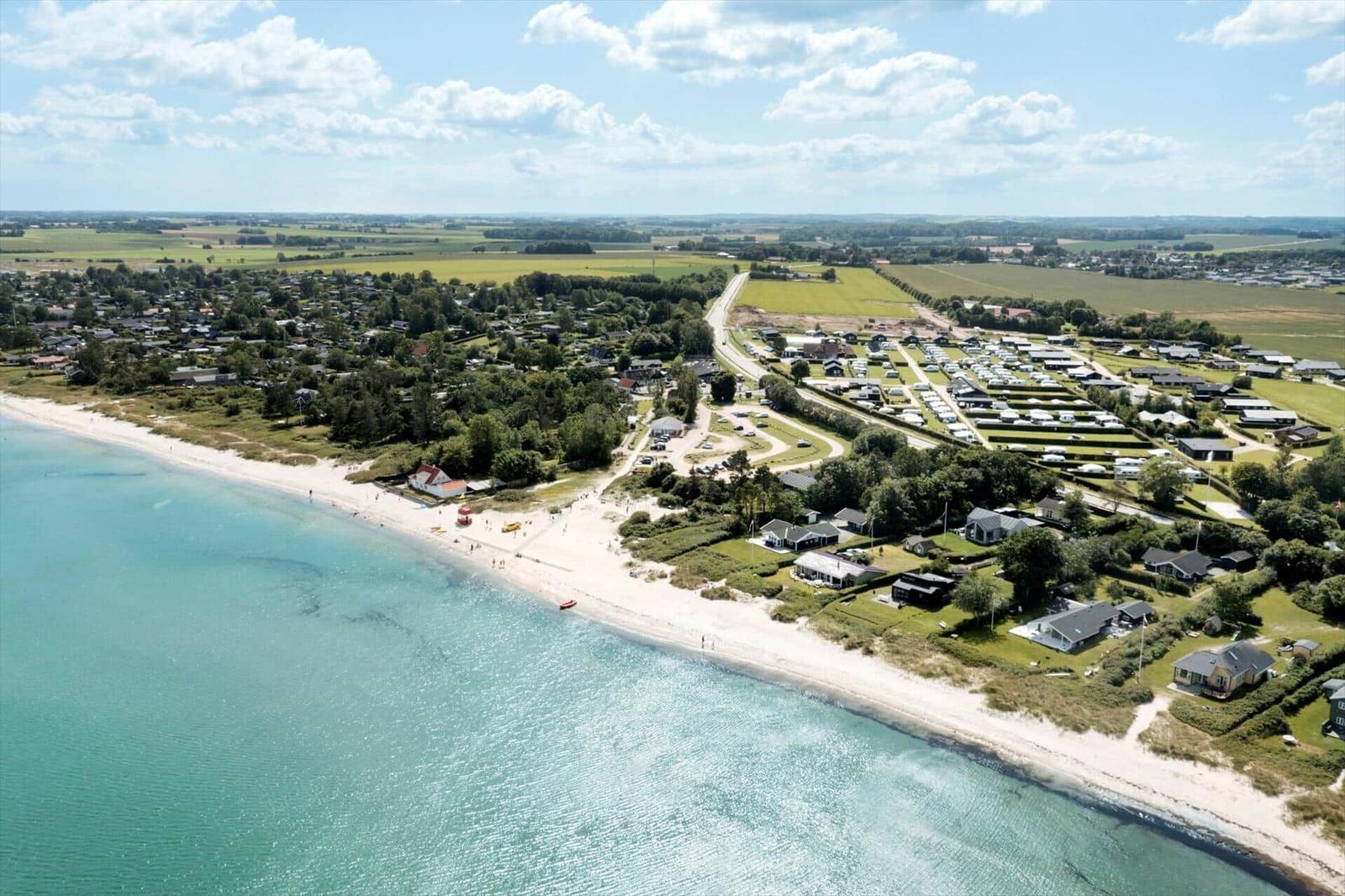 Beach with white sand and clear water, surrounded by houses and green areas.