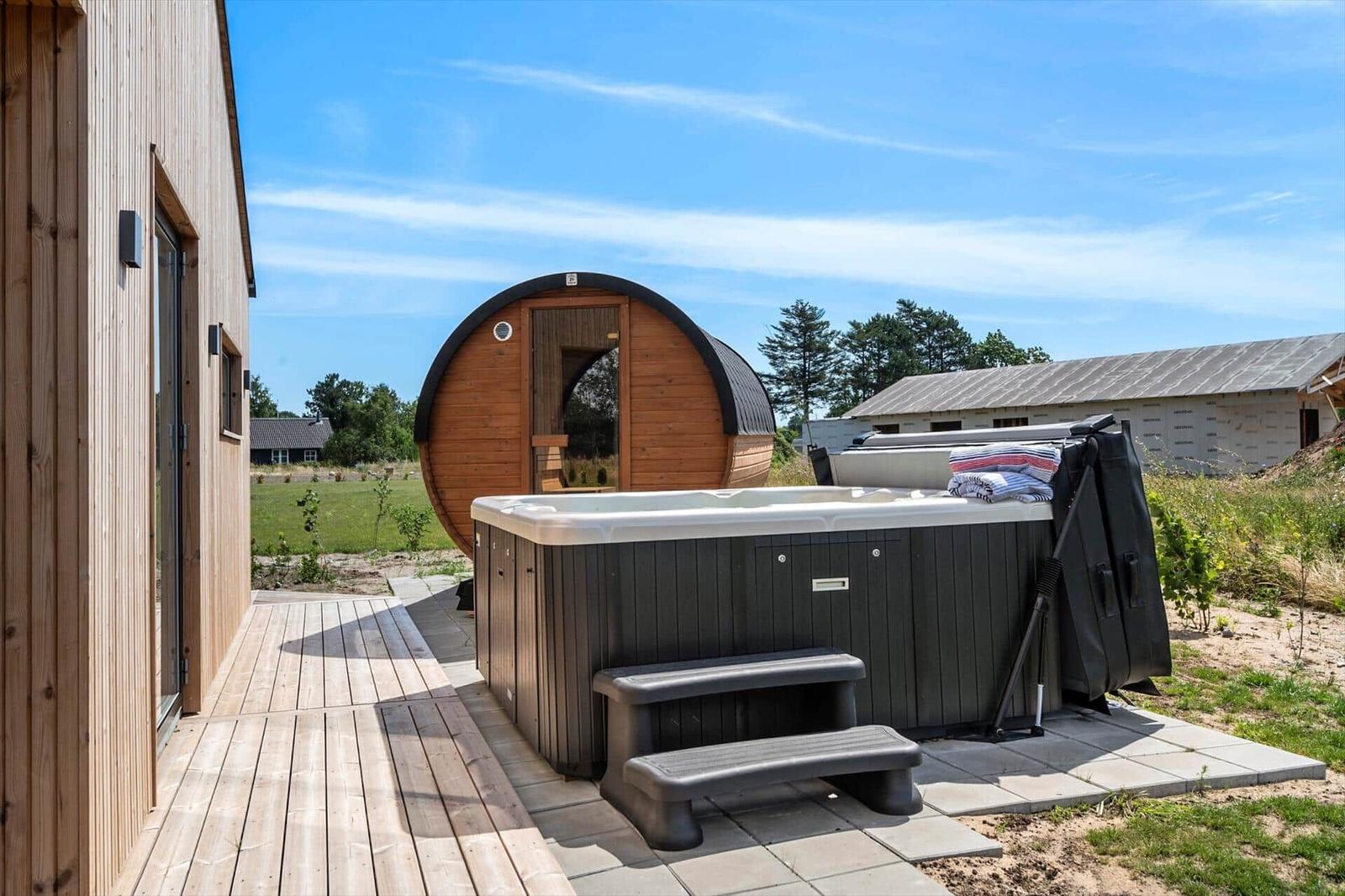 Outdoor area with hot tub and wooden sauna. Wooden deck and view of green landscape.