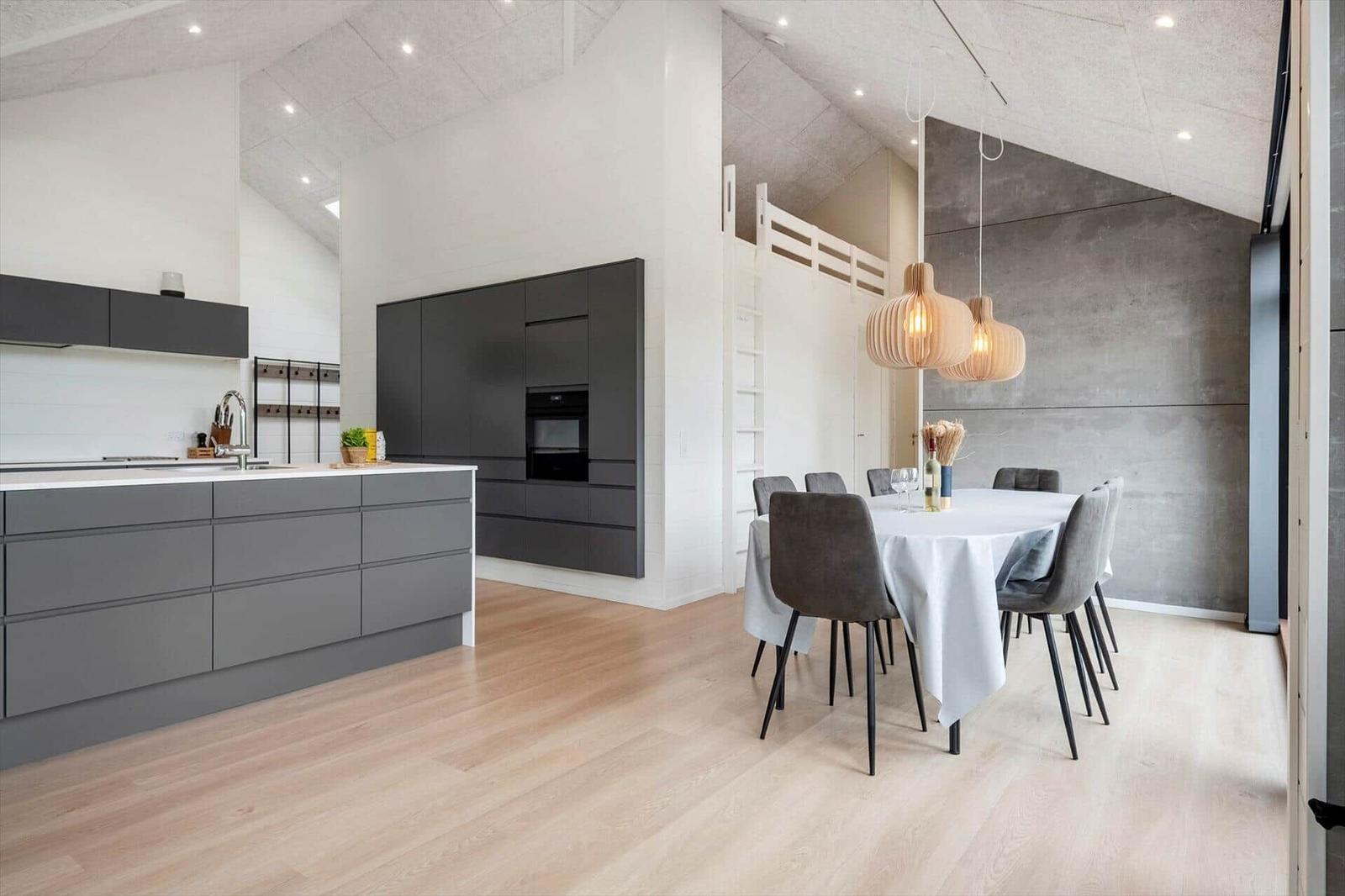Moderne Küche mit Essbereich und Holzboden. Hängelampen und graue Stühle.